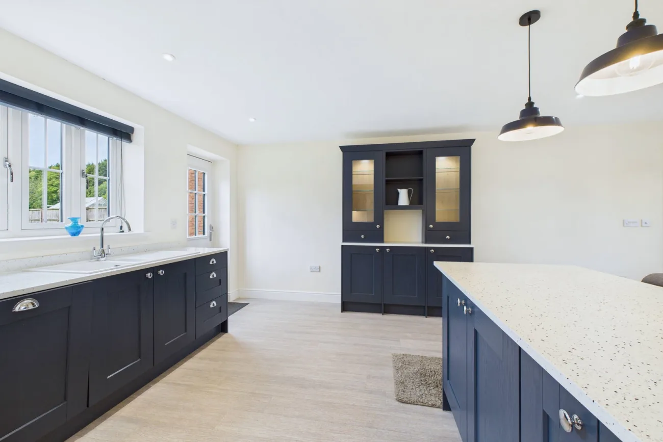 The kitchen-diner from the dining end, showing the navy peninsula breakfast bar with industrial pendants overhead