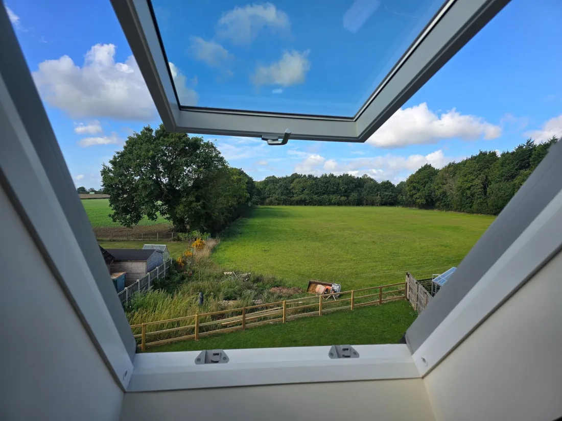 The view east through a Velux window from the second floor — open Norfolk fields, treeline and a clear sky