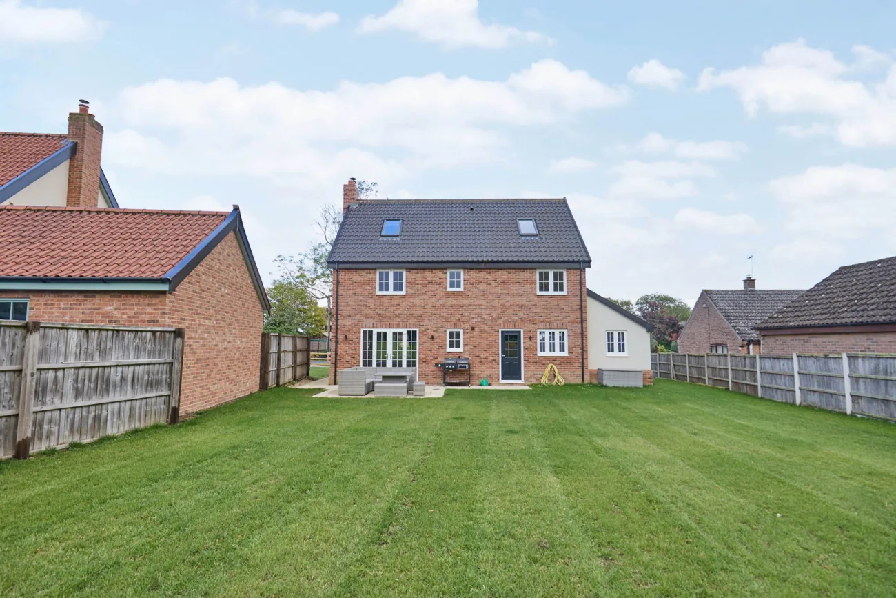 The rear elevation of the home from the garden, brick-built with white-painted detail and the detached double garage to one side