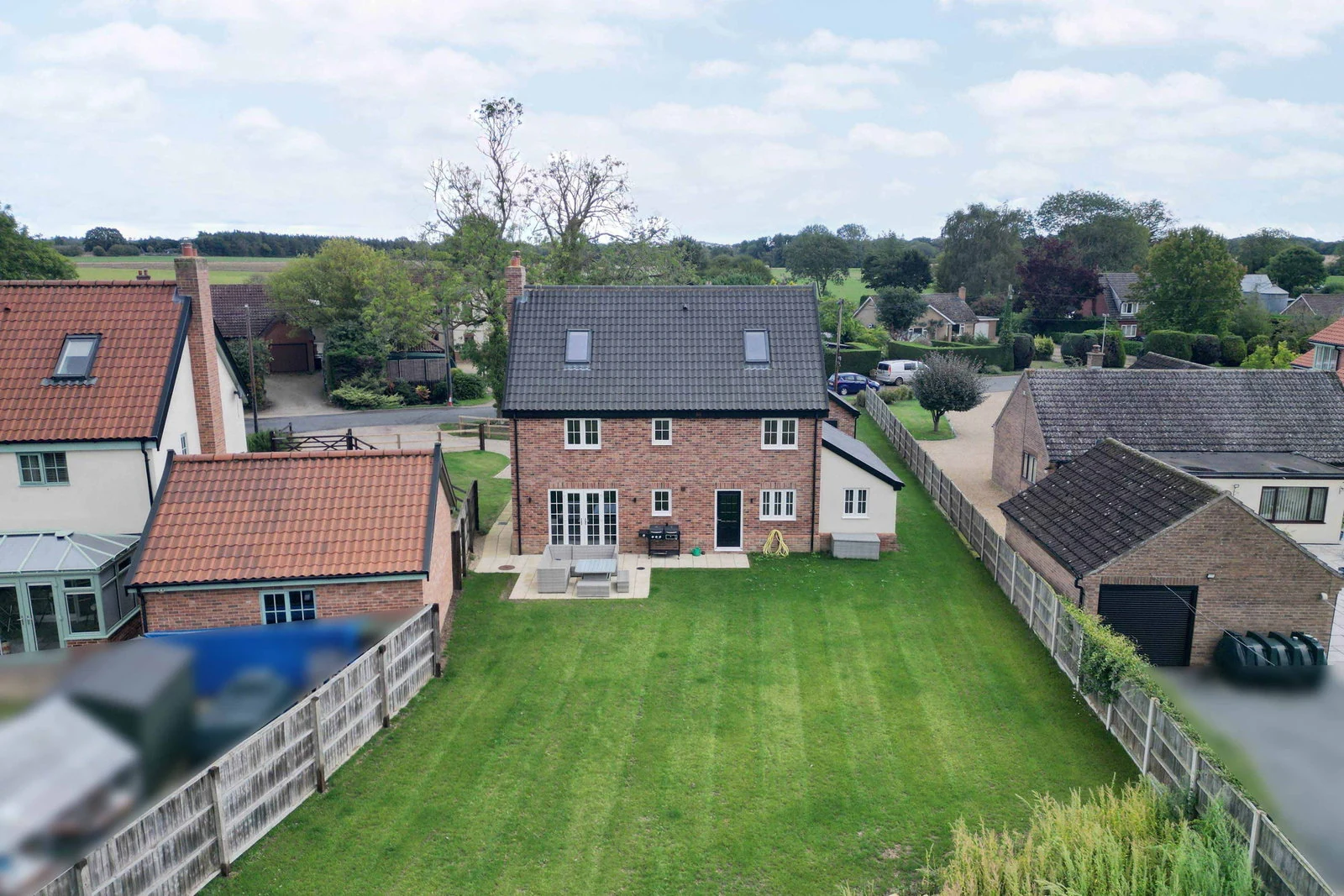 An aerial drone view of the home from the rear, showing the lawn, paved patio, detached double garage and open Norfolk fields drawing east