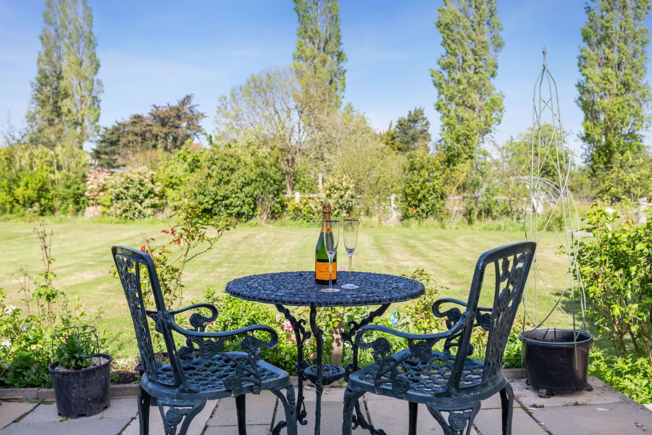 A cast-iron bistro set on the west-facing patio, lawn and mature shrubs beyond.