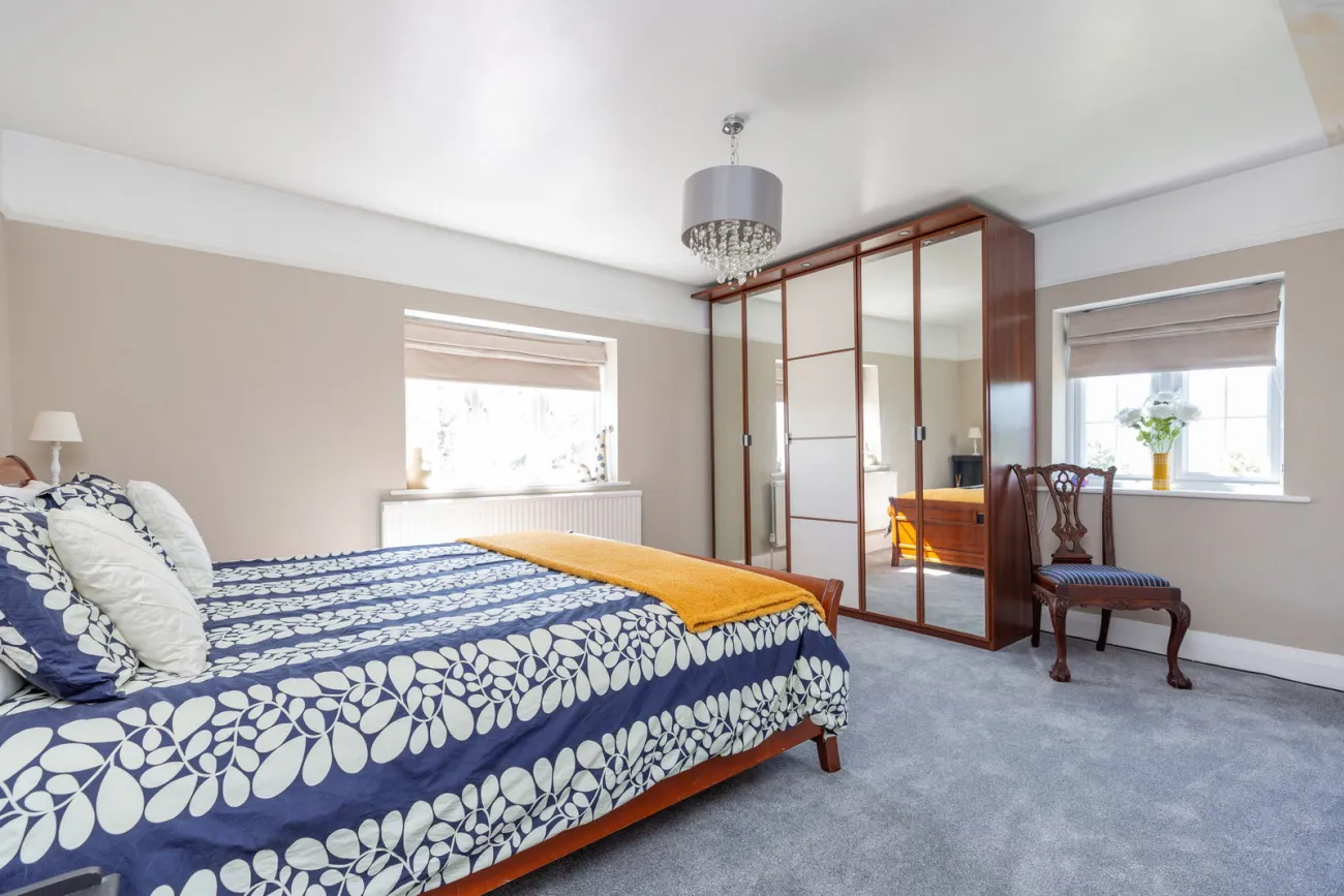 Guest bedroom with cream walls, mirrored mahogany wardrobes, and a deep window seat.
