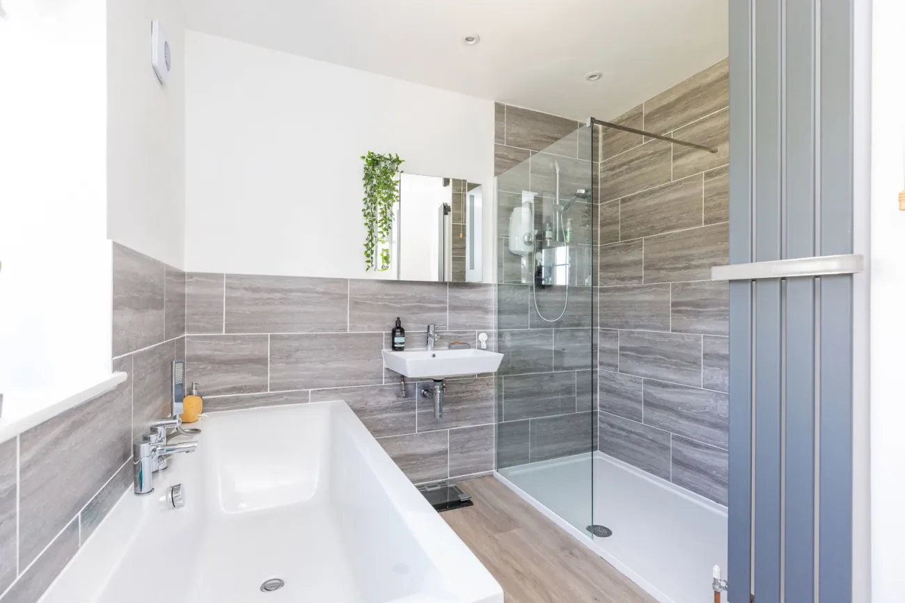 Family bathroom with white bath, walk-in shower, and stone-tone tiling.