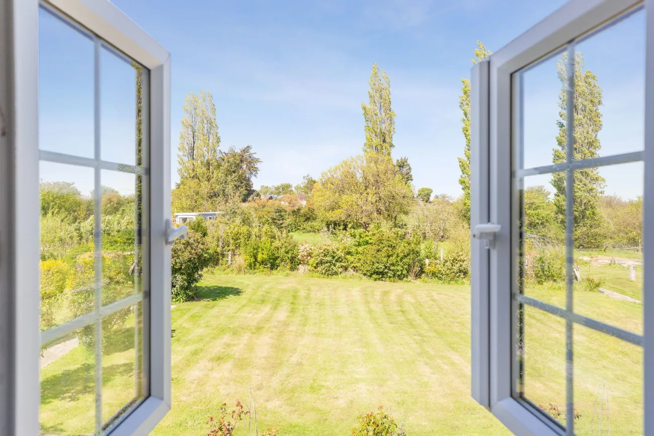 Open French doors framing the garden — lawn, mature trees, and far hedgerow beyond.