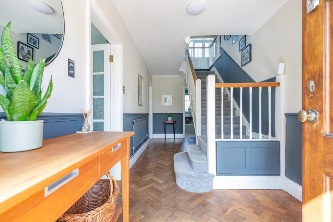 The hall and stair, parquet running through, dark blue dado picking up the panelling.