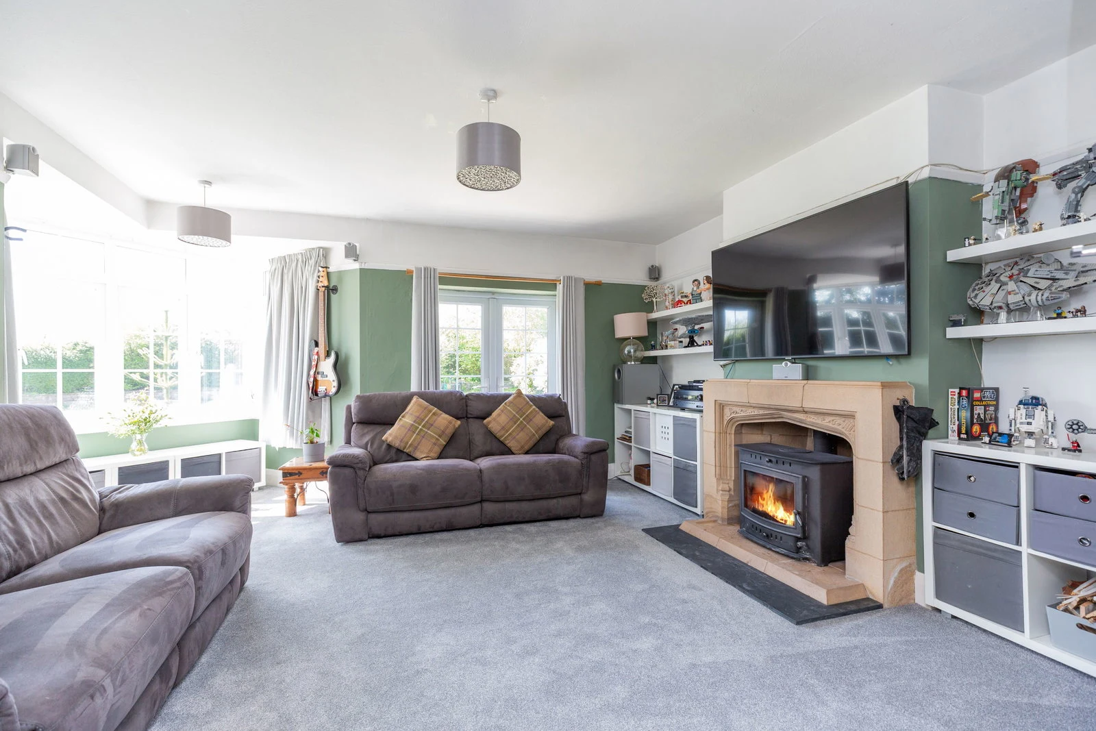 The living room with a wood burning stove in a feature stone surround and a soft green feature wall.