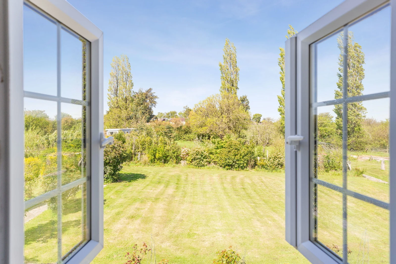 Open French doors framing the garden — lawn, mature trees, and far hedgerow beyond.